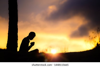 Silhouette of young male christian sitting and praying to god with light of sunset background, christian hope concept.