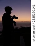 Silhouette of young male photographer at twilight capturing the sunset