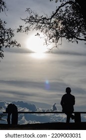 Silhouette Of Young Man Drinking Can Of Beer Alone On Bench And Watching Beautiful Scenery During Twilight Before Sunset Alone And Enjoying Beer Break On Blurry Background Of Beautiful Scenery.