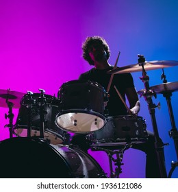 Silhouette of young man drummer playing isolated on blue-pink background in neon