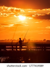 Silhouette Of A Young Man Fishing Off A Pier As The Sun Sets In The Background. Jones Beach, Long Island