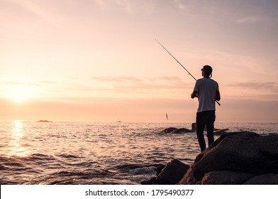 Silhouette of a young man fishing, spining style, from the rocks at the galician coast, in front of the Atlantic Ocean while the sun goes down. Magic moment to get better fishes - Powered by Shutterstock