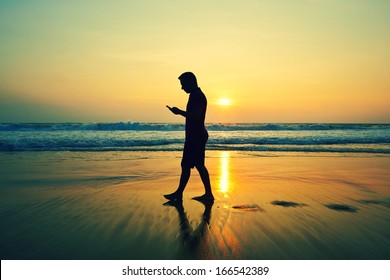 Silhouette Of Young Man With Mobile Phone On The Beach At Sunset 