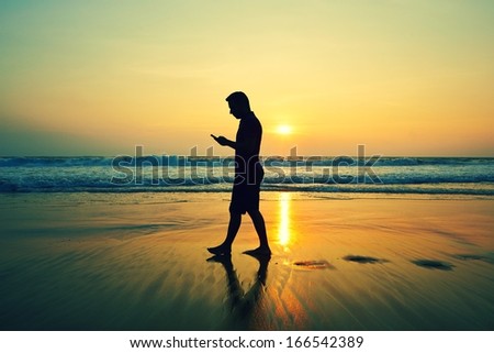 Silhouette of young man with mobile phone on the beach at sunset 
