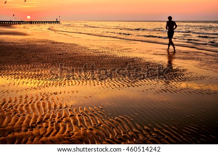 Silhouette of young man running on beach sand at sunrise. Original wallpaper from summer active vacation.