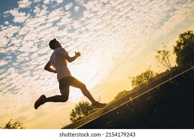 Silhouette Of Young Man Running Sprinting On Road. Fit Runner Fitness Runner During Outdoor Workout With Sunset Background.