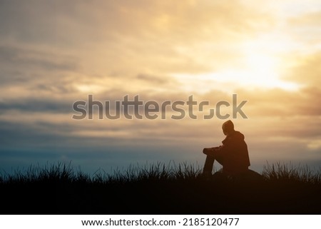 Silhouette of young man sits praying alone at the top of the mountain at sunset with beautiful natural sunlight.