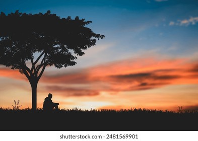 Silhouette of young man sitting and praying alone under the big tree at sunset with beautiful sky and natural sunlight. - Powered by Shutterstock