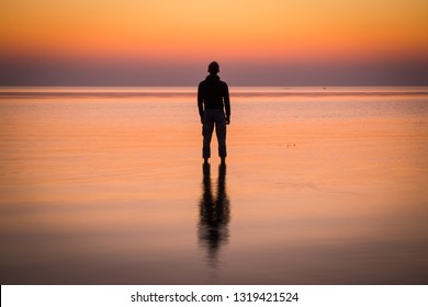 Silhouette of young man staying in the calm water of the sea. Sunset.