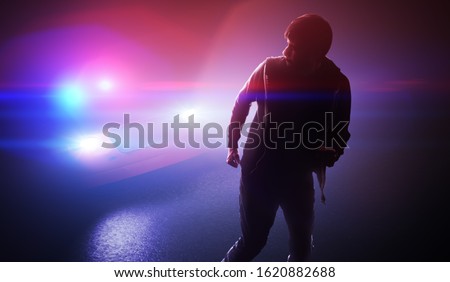 Silhouette of young man - thief escaping from police car at night.