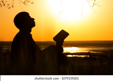 silhouette of young man turns to God with questions about life sitting under tree on the lawn, male on the nature looking up at the sky with fatigue and the hope, the concept of faith and spirituality - Powered by Shutterstock