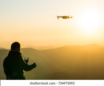 Silhouette of young man using drone at sunset for photos and video making - Happy man having fun with new technology trends in mountains