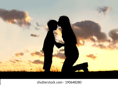 Silhouette of a young mother lovingly kissing her little child on the forehead, outside isolated in front of a sunset in the sky on a summer day.