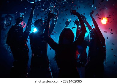 Silhouette of young people with raised flutes having fun and clubbing