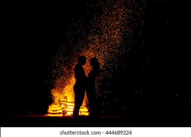 Silhouette of young people who are standing in front of fire and holding each other