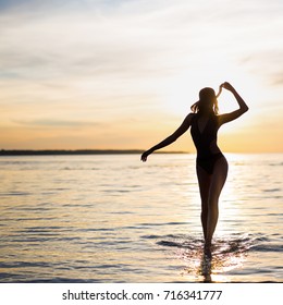 silhouette of young sexy woman in bikini walking on the beach at sunset
