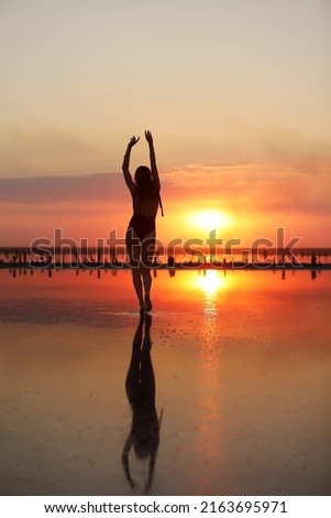 silhouette of a young slim woman in a swimsuit who dancing at sunset on the sea. summer holiday.