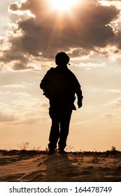 Silhouette Of Young Soldier In Military Helmet Against The Sun