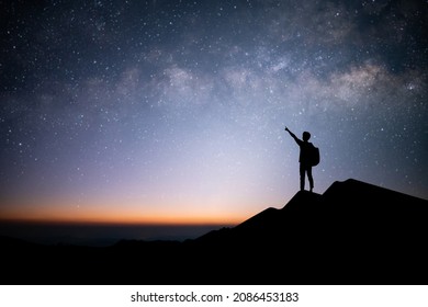 Silhouette of young traveler and backpacker raise your hand and point your finger at the stars and milky way in the sky. He enjoyed traveling and was successful when he reached the summit. - Powered by Shutterstock