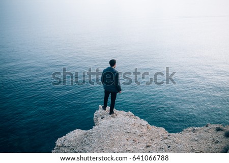 Silhouette of a young traveller and adventurer standing on a cliff staring into the deep dark water with a soft shadow gradient
