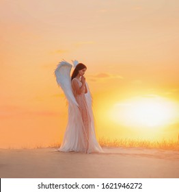 Silhouette young woman angel stands in desert praying. Creative glamour design costume clothes with bird wings feathers. Bright yellow color sunset dramatic heaven. Photo Shoot Divine Fairy Spirit