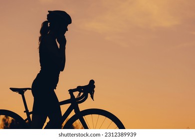 Silhouette of a young woman cyclist adjusting her helmet and preparing for riding road bicycle on a free road during a sunset. Healthy lifestyle concept. Copy space. - Powered by Shutterstock