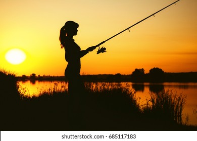 Silhouette of a young woman engaged in sport fishing on the river bank at dawn in the picturesque nature - Powered by Shutterstock