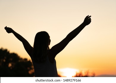 silhouette of young woman with open arms raised in a sunset - Shutterstock ID 1489279166