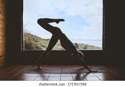 Silhouette Of Young Woman Practicing Yoga Indoor On Background Of Big Window With Natural Landscape. Girl Doing Vinyasa Yoga Flow Practice On Yoga Mat. Female Health Of Body And Mind, Relax At Home.