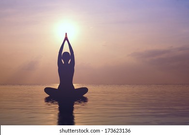 Silhouette young woman practicing yoga on the beach at sunset