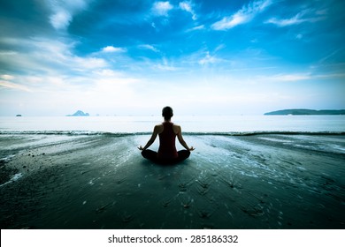 Silhouette young woman practicing yoga on the beach