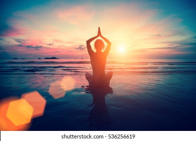Silhouette young woman practicing yoga on the beach at sunset. Meditation. - Shutterstock ID 536256619