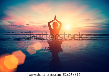 Silhouette young woman practicing yoga on the beach at sunset. Meditation.