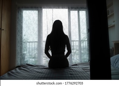 silhouette of a young woman sitting on a bed spending time alone at home, young upset pensive woman feeling lonely or frustrated thinking about problems - Powered by Shutterstock