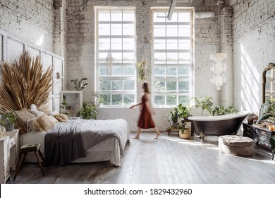 Silhouette Of Young Woman Walking At Home With Interior Design In Bohemian Style Against Loft Brick Wall With Large Windows. Dreamy Female Standing Between Cozy Bed In Bedroom And Bathroom Bath