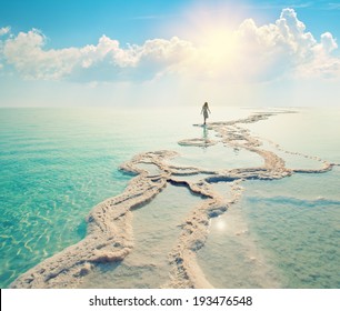Silhouette of a young woman walking on Dead Sea salt shore at sunrise towards the sun. Solitude
