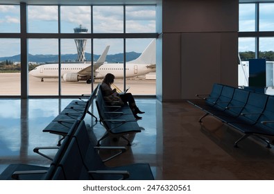 Silhouette of young woman working on laptop and waiting for flight in the Airport - El Prat-Barcelona airport. This airport was inaugurated in 1963 - Barcelona, Spain  - Powered by Shutterstock