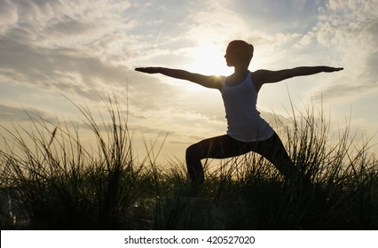 Silhouette of a young woman in a yoga warrior pose on a beach hilltop