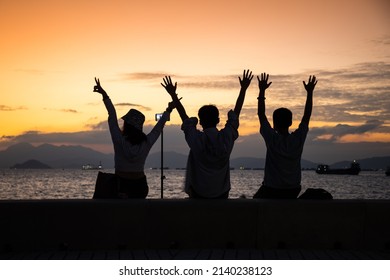 Silhouette Of Youngsters Students Boy And Girl Chat And Have Fun And Take Selfie Of Mobile Phone Camera During Sunset In West Kowloon Waterfront Promenade, Hong Kong In Evening. Back Light Shot