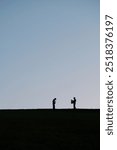 Silhouetted against a clear evening sky, two figures stand on top of Citadel Hill in Halifax, Nova Scotia. One person appears to be looking through a camera while the other poses.