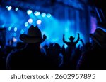 Silhouetted audience with cowboy hats at a country music concert under dynamic blue lighting.