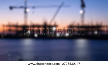 Silhouetted construction cranes and building frames against a vibrant sunset sky, with blurred city lights in the foreground.
