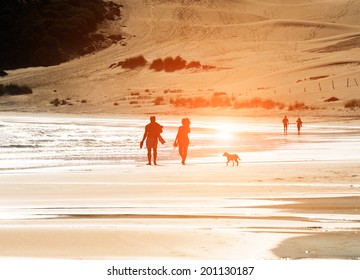 Silhouetted Couple Walking A Dog On The Beach