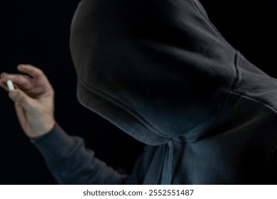 Silhouetted Figure in Dark Hoodie Holding a Pill Against a Black Background, Mysterious and Dramatic Lighting - Powered by Shutterstock