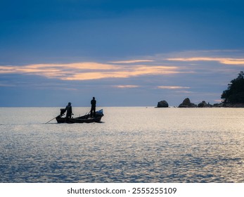 Silhouetted fishermen navigate calm waters at dusk, a serene scene of coastal life and twilight beauty at Ao Manao beach,Narathiwat,Thailand
 - Powered by Shutterstock