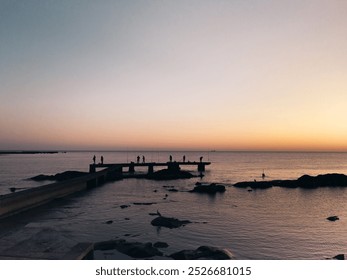 Silhouetted fishermen on a dock at sunset by the sea. - Powered by Shutterstock