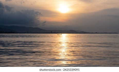 Silhouetted fishermen in small wooden fishing boat canoe with beautiful golden sunlight reflecting over surface of ocean water on the tropical island of Timor-Leste in Southeast Asia - Powered by Shutterstock