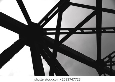 Silhouetted geometric steel beams form an intersecting web against an overcast sky, creating a stark contrast with dramatic lines. - Powered by Shutterstock