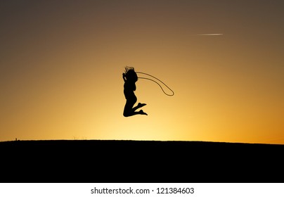 silhouetted girl rope skipping in sunset