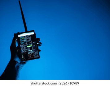 Silhouetted hand holding a hacking device against a blue-lit background, creating a modern and tech-inspired aesthetic - Powered by Shutterstock